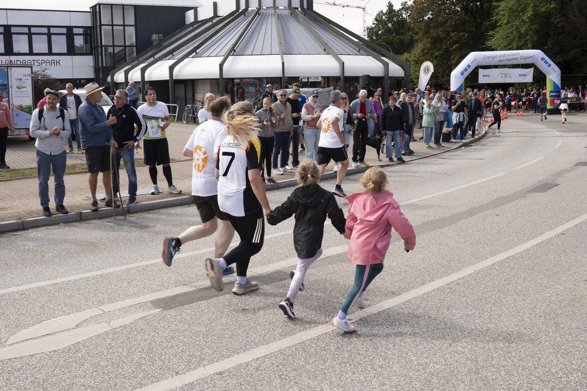 Zwei Kinder laufen gemeinsam mit Erwachsenen &uuml;ber die Stra&szlig;e Richtung Ziel, im Hintergrund der ews-Zielbogen.